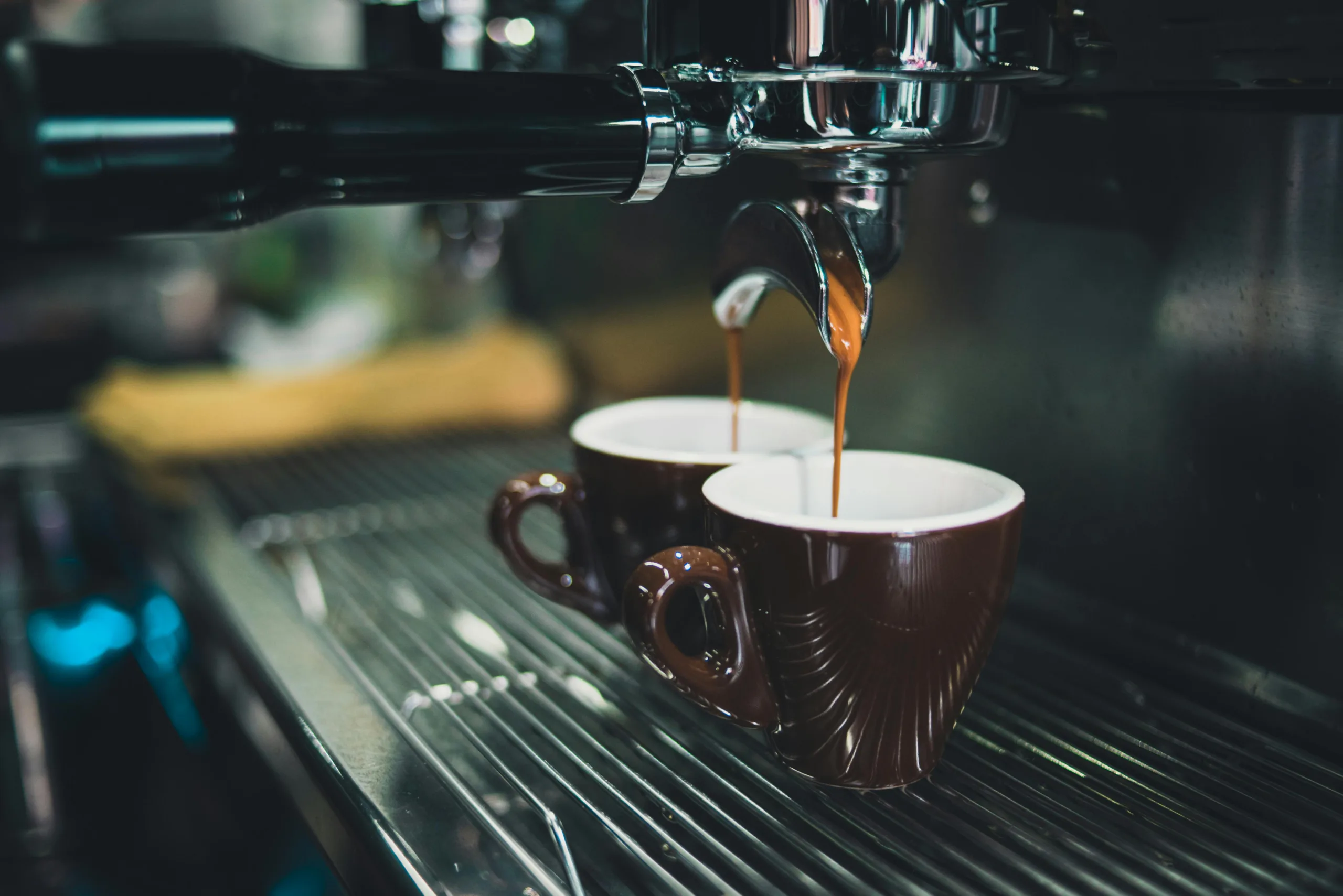 Fresh espresso flowing from a commercial espresso machine into two ceramic cups.